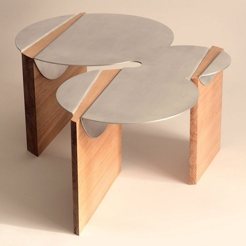 A photograph of a table, with a silver tabletop in abstract circular shapes atop three brown wooden legs.