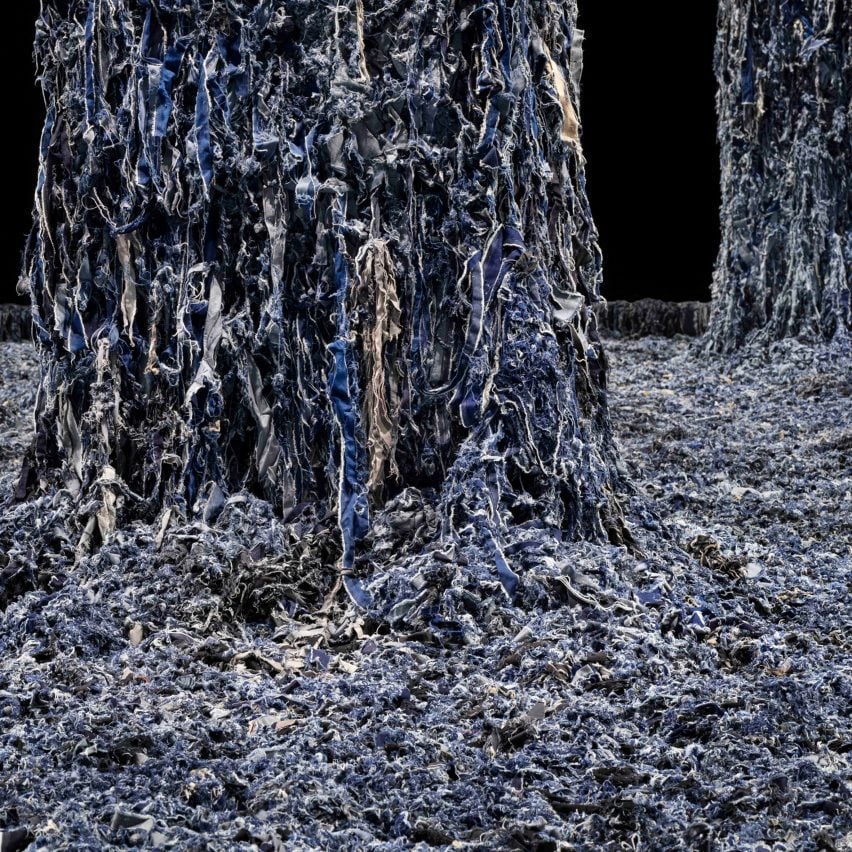 A close up photograph of a large floor covered in blue denim scraps, with two columns emerging from it, also covered.