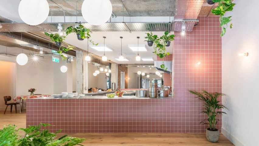 Photograph of a communal interior space with a pink tiled partition and circular lights hanging from the ceiling.