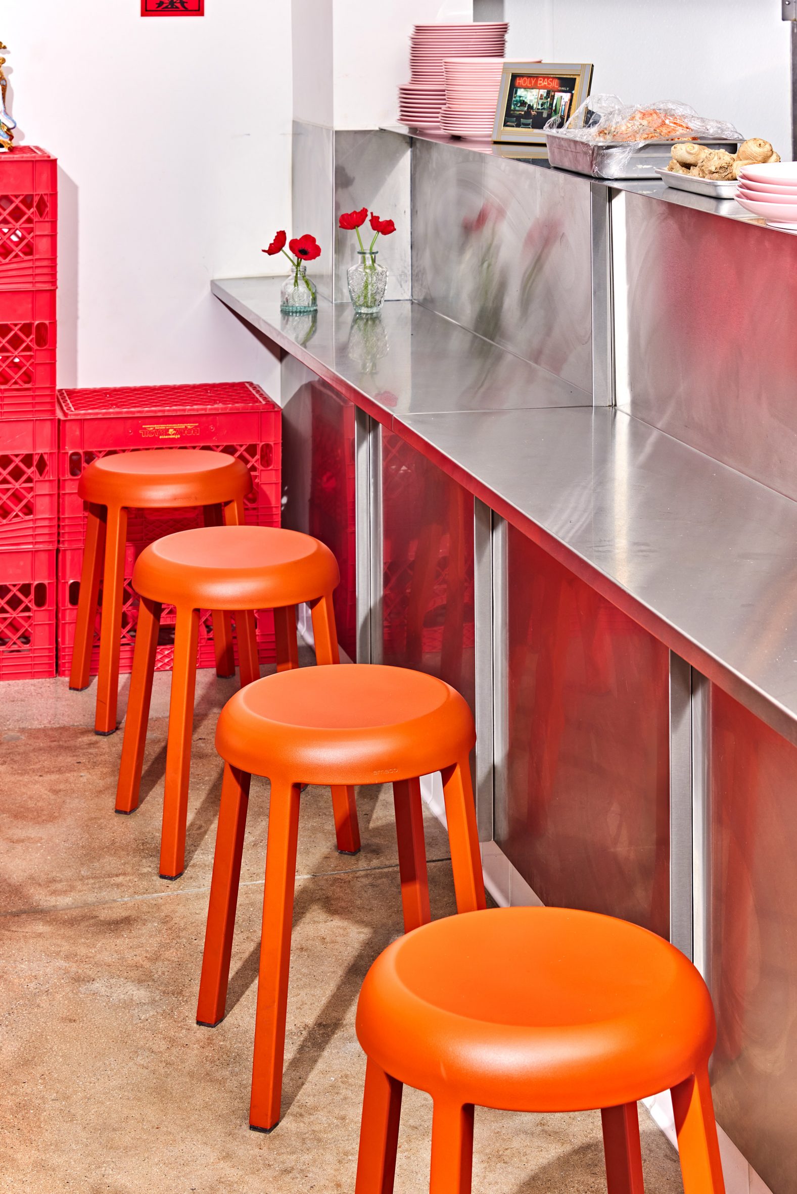 Stainless steel service counter with a low shelf accompanied by red stools