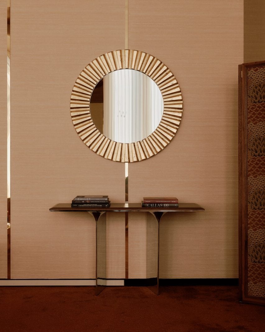 Textured wallpaper between vertical strips of polished brass behind a circular mirror