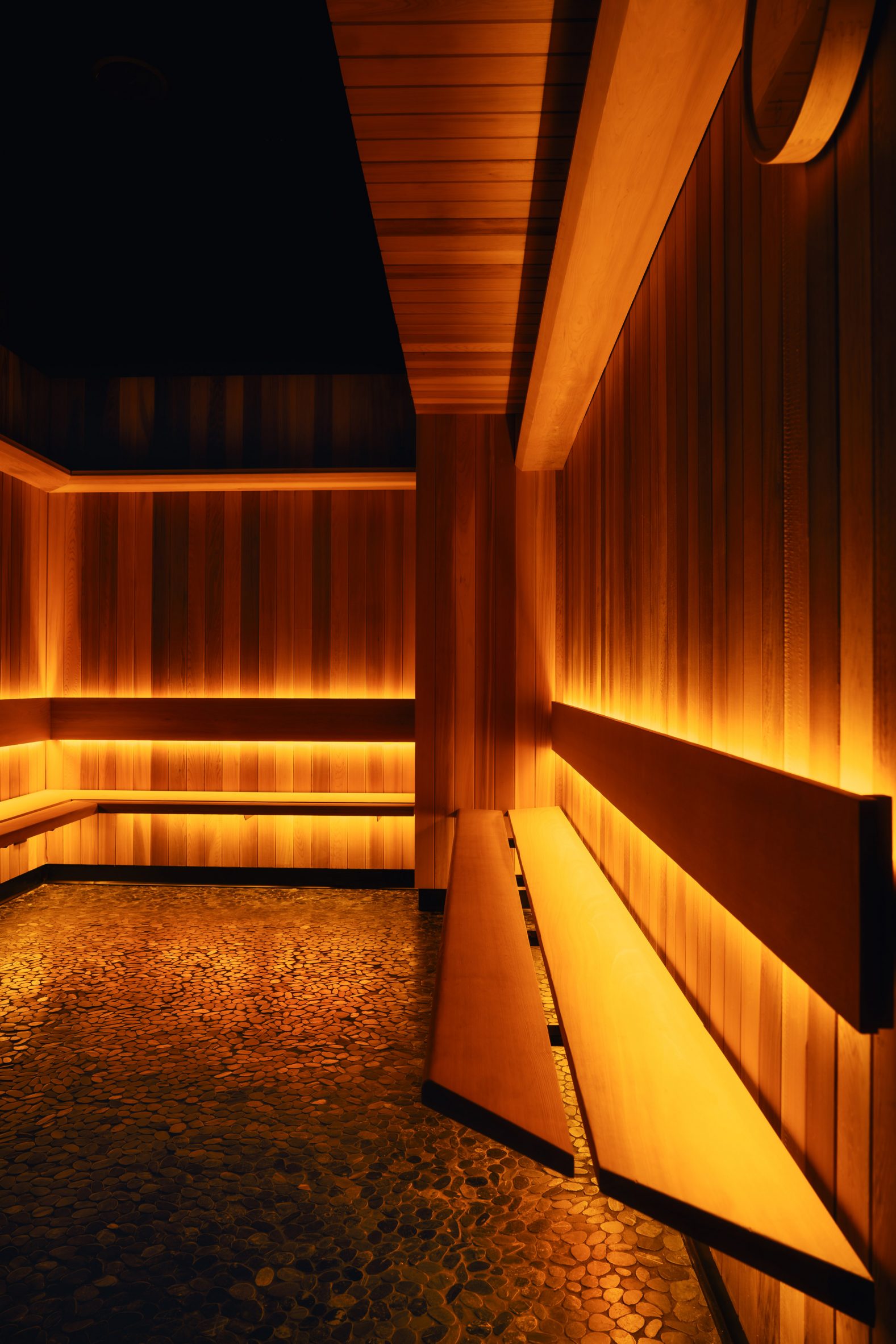 Sauna with panelled walls, pebble flooring and soft lighting