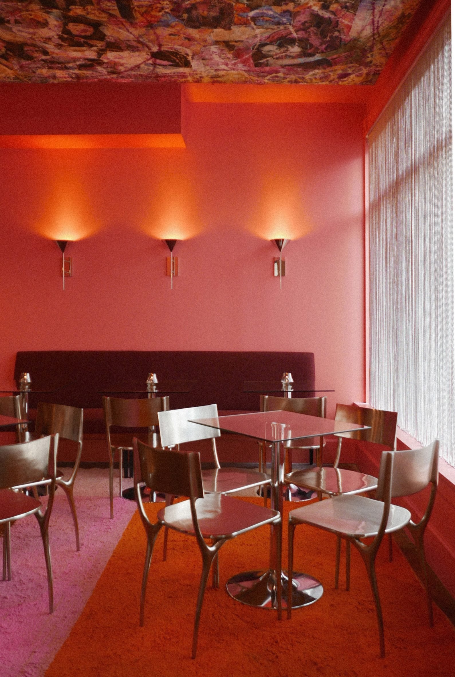 Small all-pink restaurant with glass tables and metal chairs