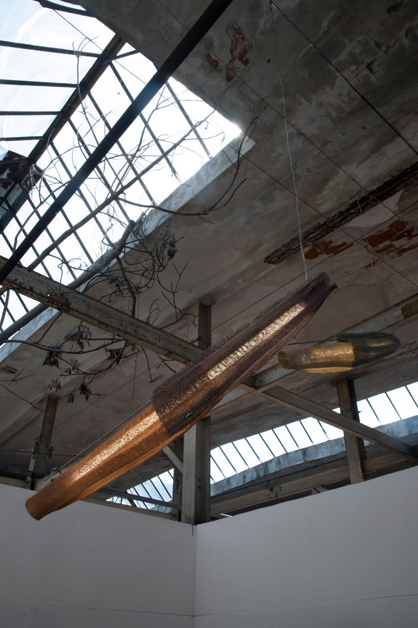 A photograph of two pendant lights in tones of orange and grey, hung diagonally from a grey concrete ceiling.