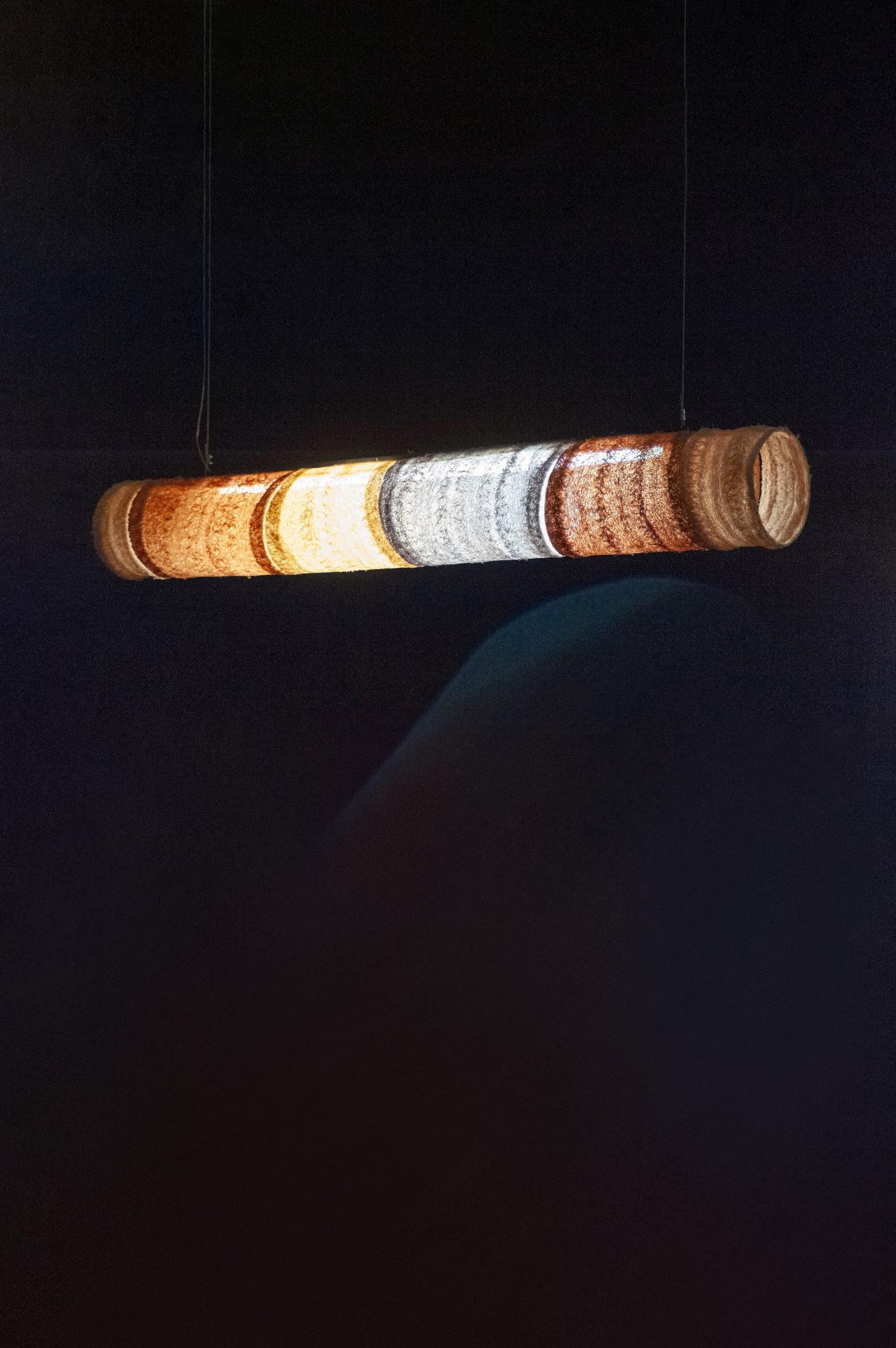 A photograph of a hanging pendant light, illuminated in darkness, in tones of orange, yellow, blue and brown.