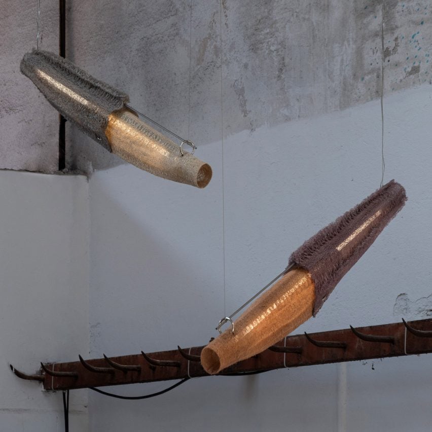 A photograph of two pendant lights, hanging diagonally, in tones of orange, beige and grey, against a white and grey concrete wall.