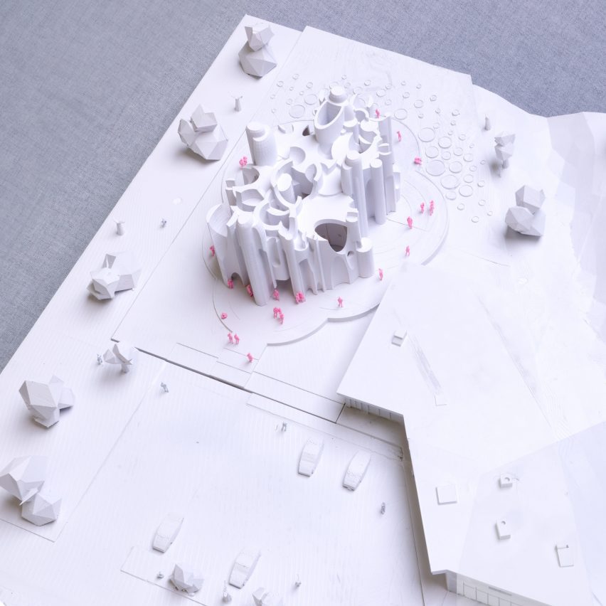 A photograph from above of a white architectural model with pink figures surrounding it.