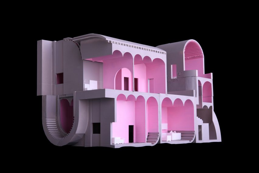 A photograph of an architectural model of a housing complex in tones of pink, against a black background.