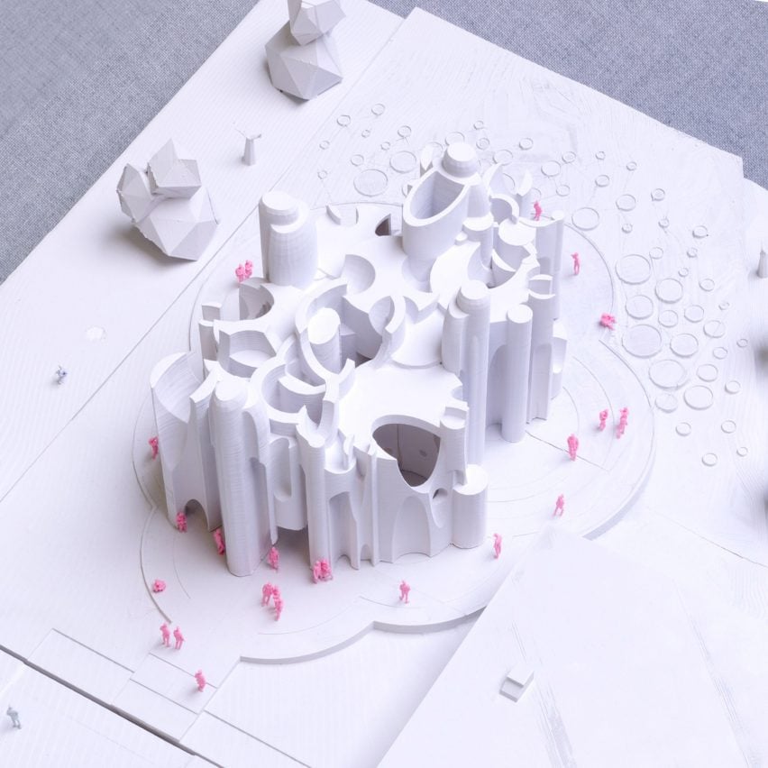 A photograph from above of a white architectural model with pink figures surrounding it.