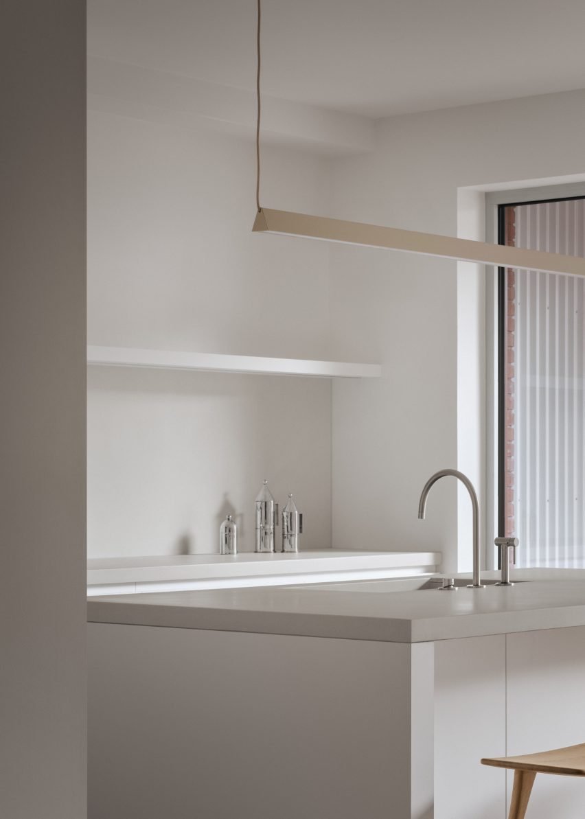 Minimalist white kitchen with floating shelf and linear light fixture above the island