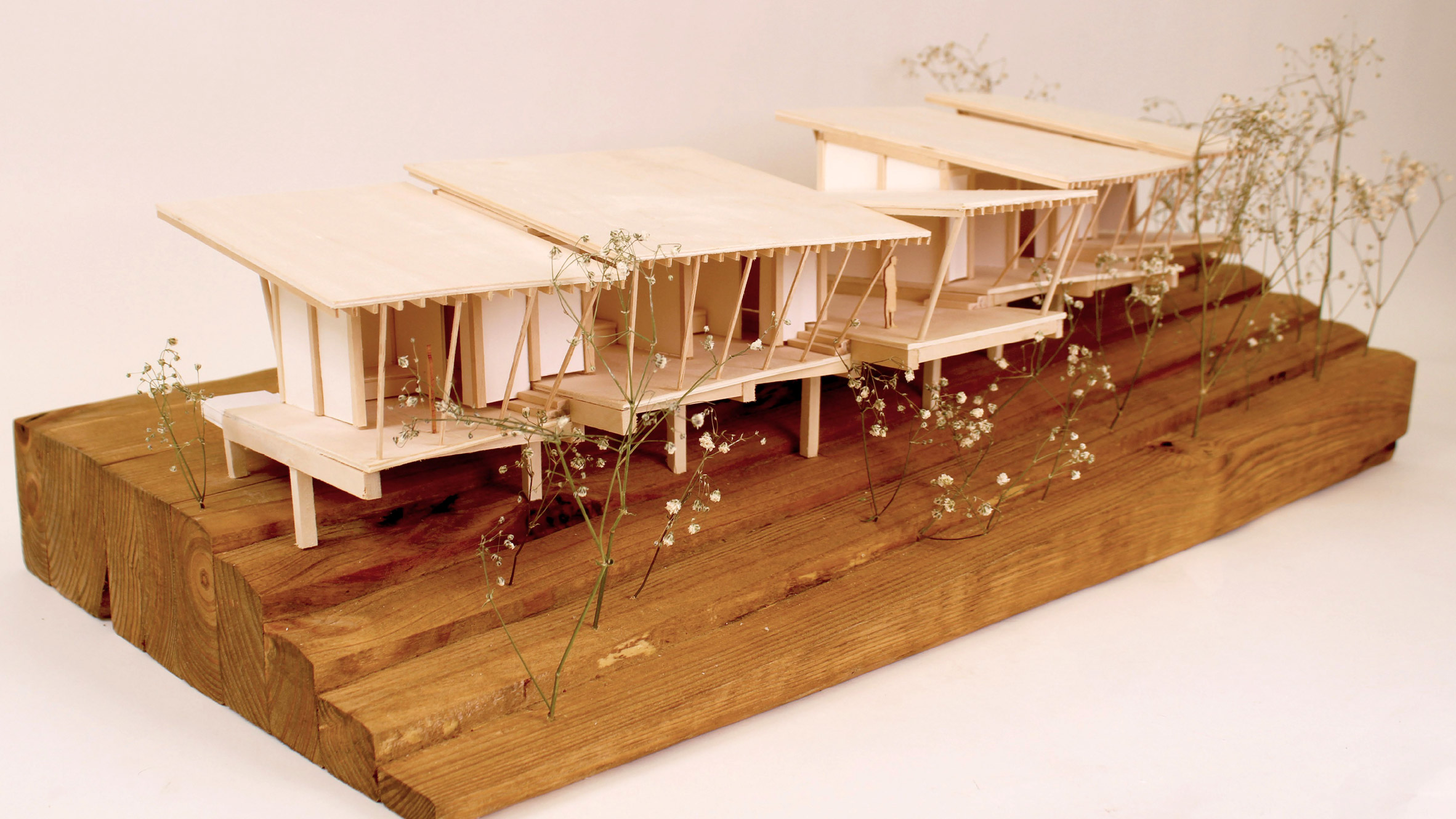 A photograph of an architectural model of a seires of huts, in tones of brown, atop a brown wooden plinth.