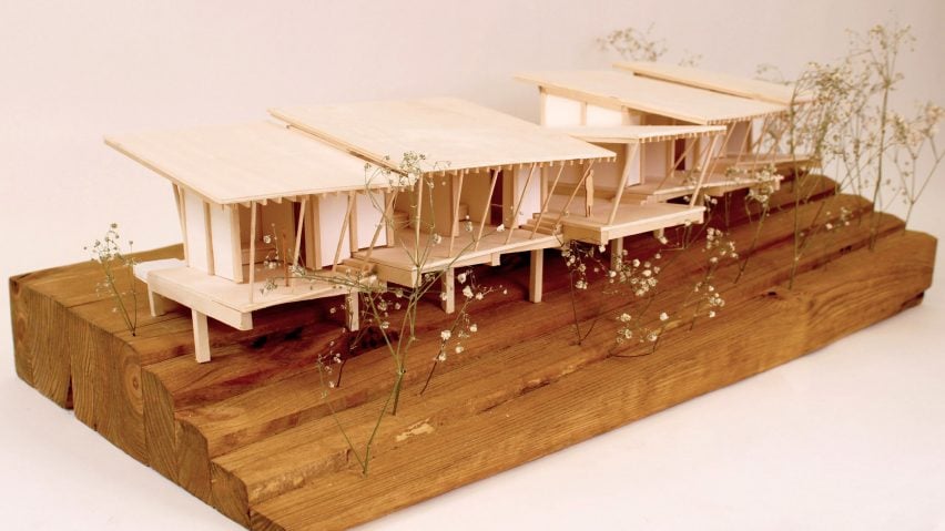 A photograph of an architectural model of a seires of huts, in tones of brown, atop a brown wooden plinth.