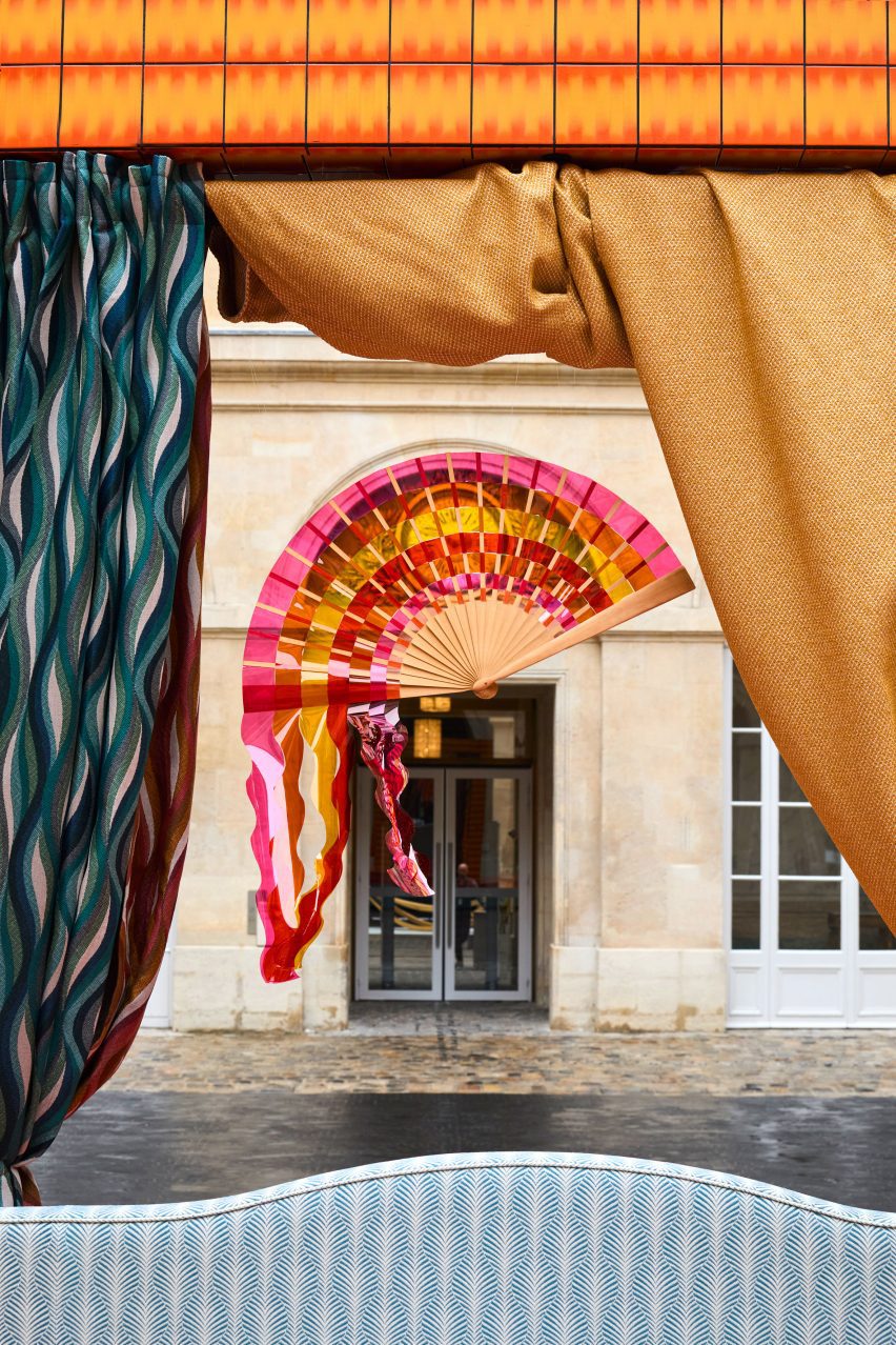 A photograph of a pink, red and yellow fan hanging from an orange structure.