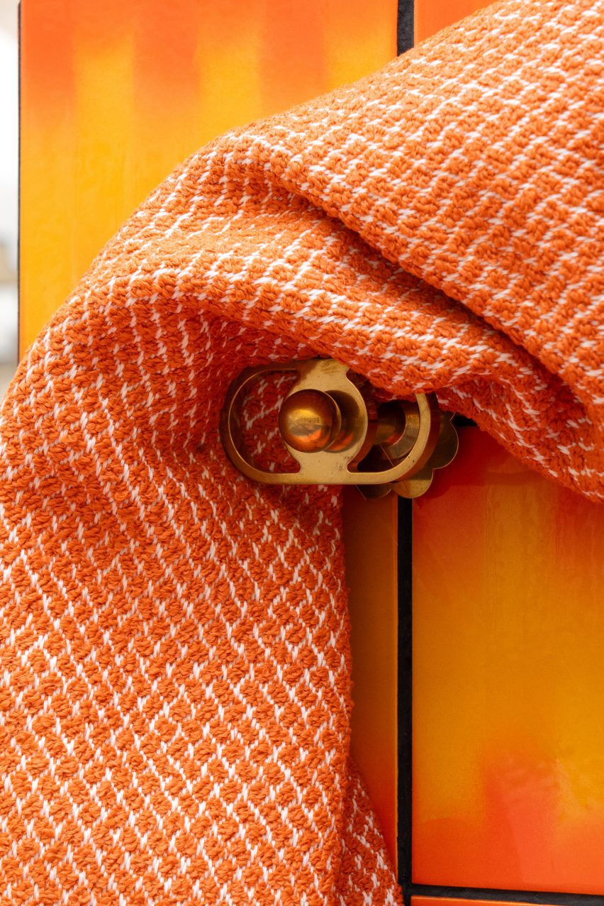 A photograph of an orange curtain draped over a golden curtain holder.