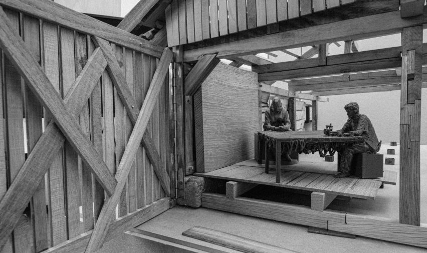 A black and white image of the inside of a wooden pavilion, with two figures sat at a table.