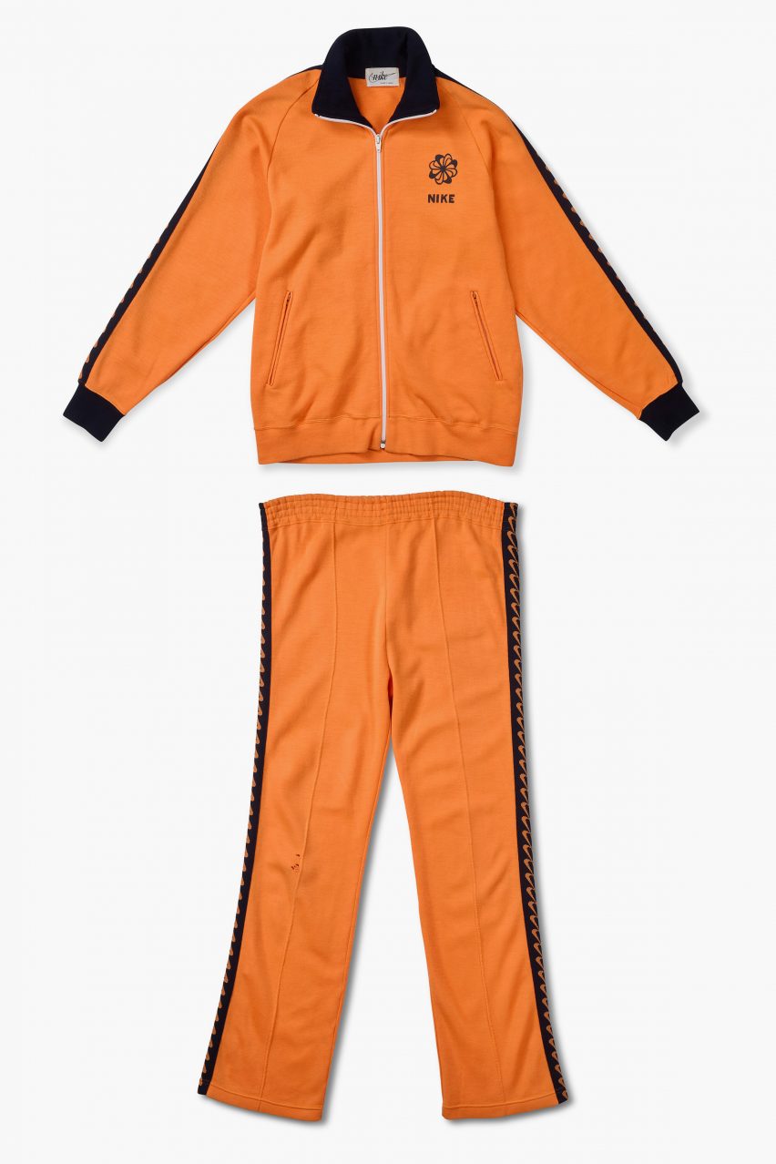 A photograph of an orange and black tracksuit set laid flat against a white background.