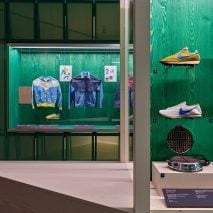 A photograph of an exhibition displaying shoes and apparel against green backdrops.