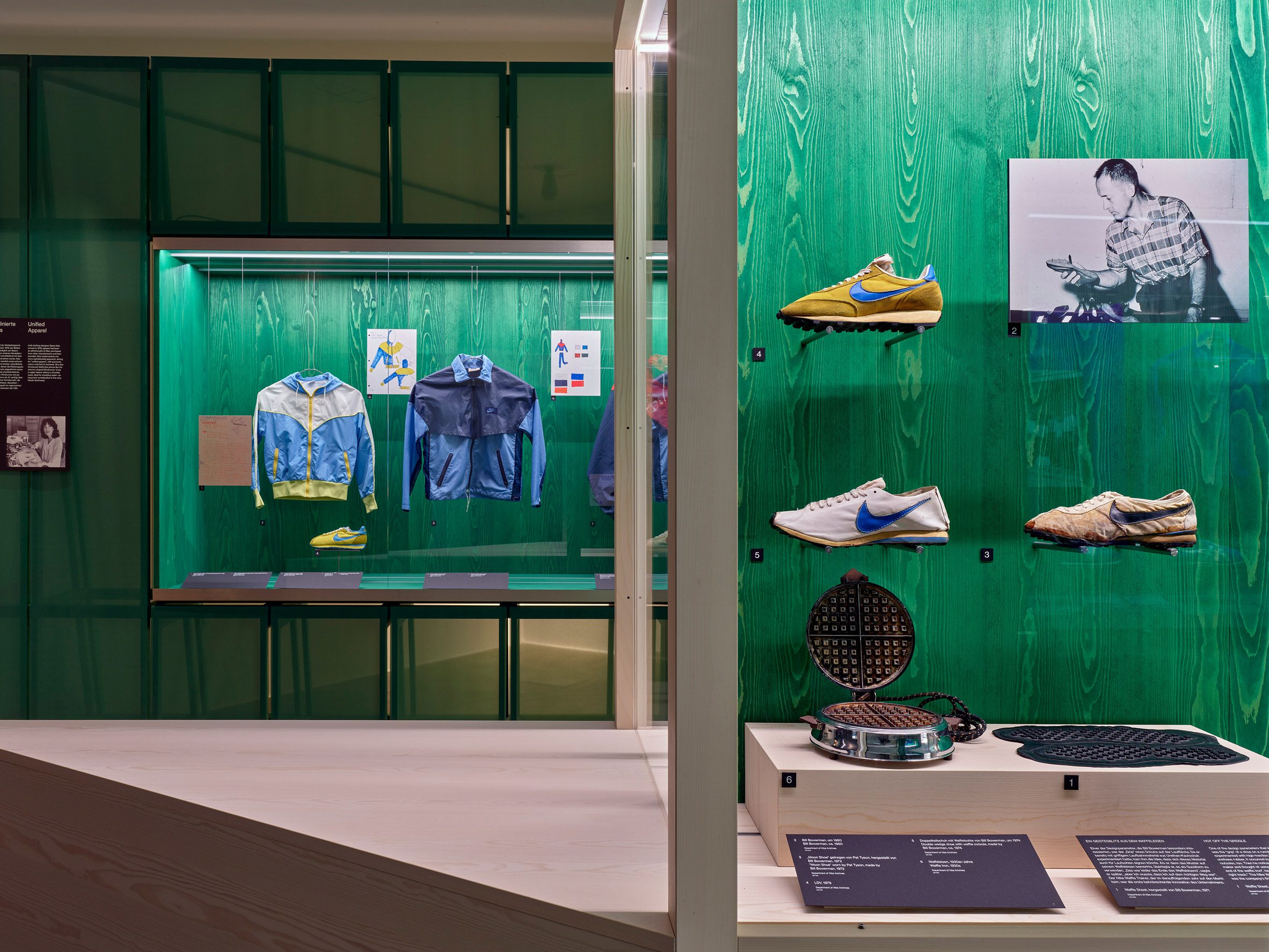 A photograph of an exhibition displaying shoes and apparel against green backdrops.