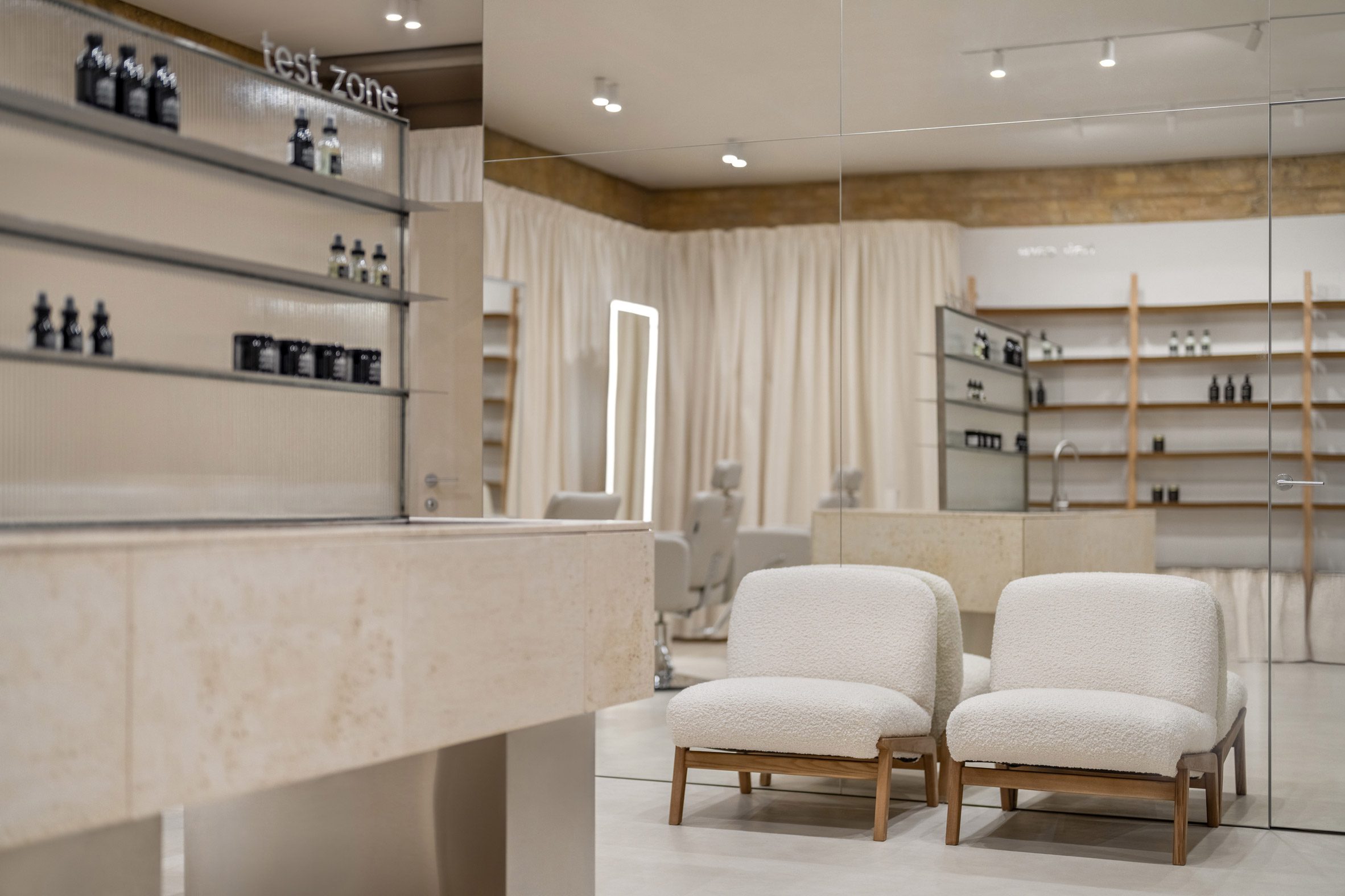 Photograph of a cosmetics showroom with neutral colours and two white armchairs.