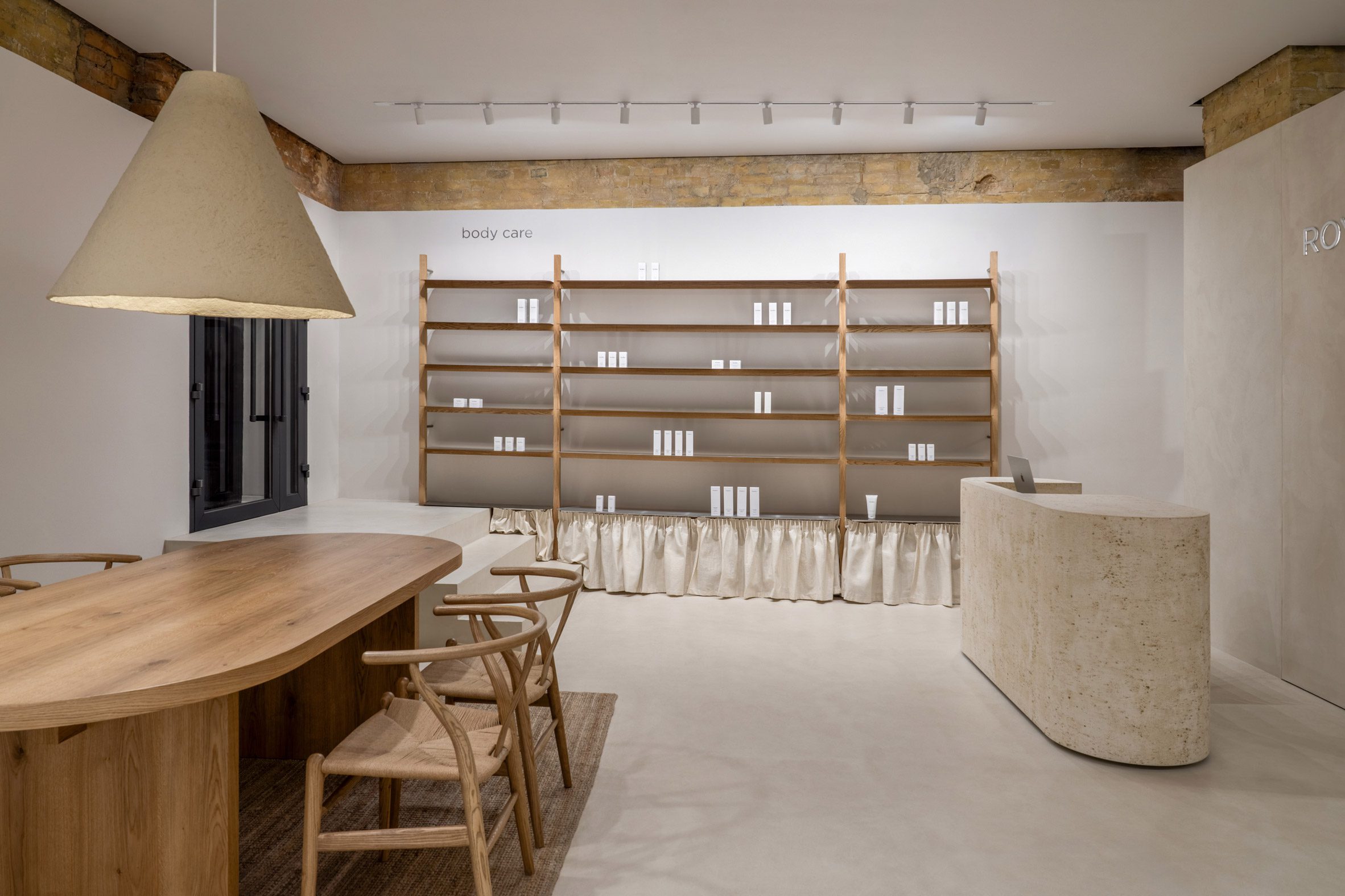 Photograph of an interior with a large wooden table and wishbone chairs on the left, a reception desk and a wooden shelving unit on the far wall.