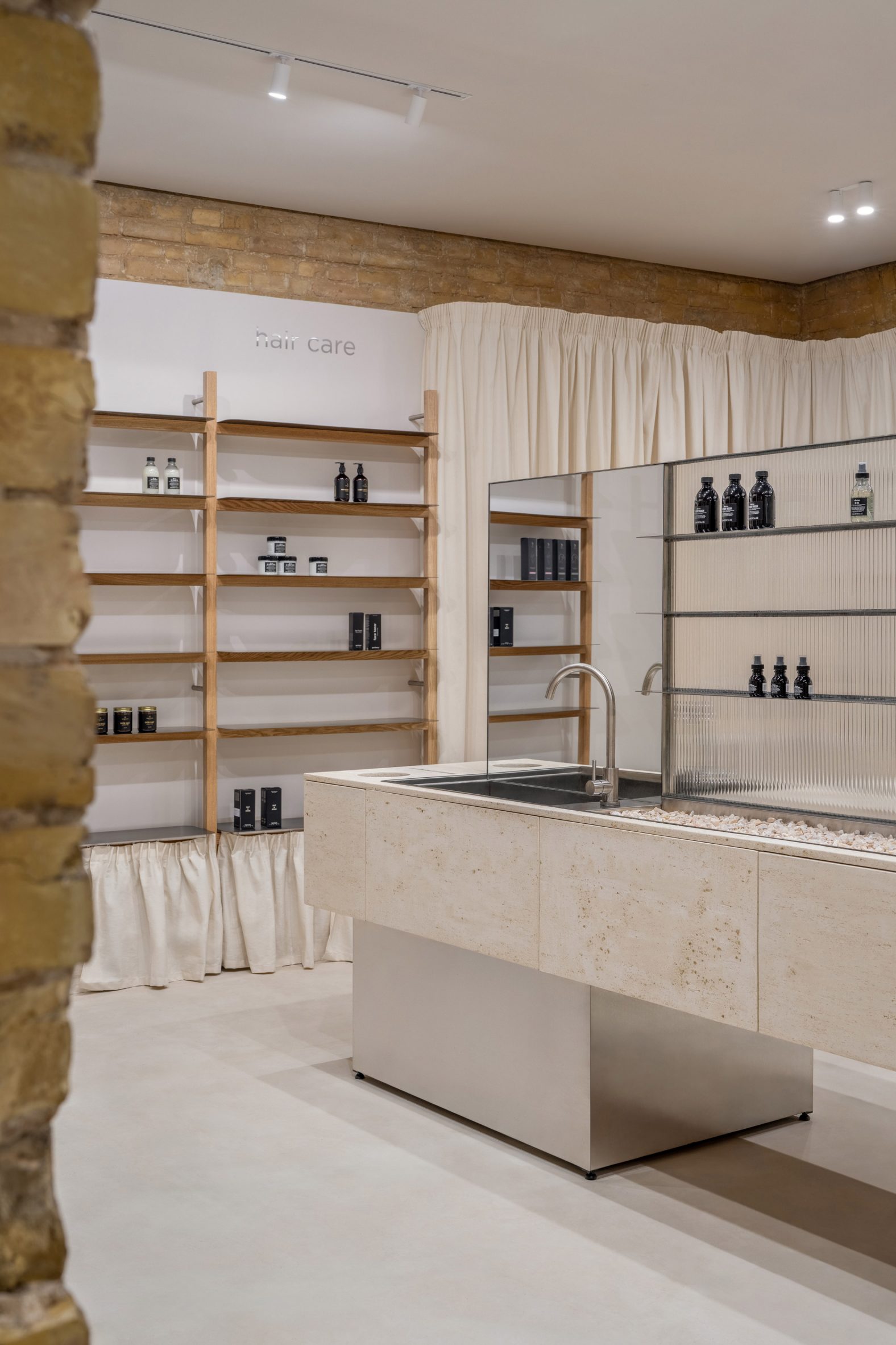 Photograph of a neutral, minimalistic showroom interior with a travertine sink and simple wooden shelving units.