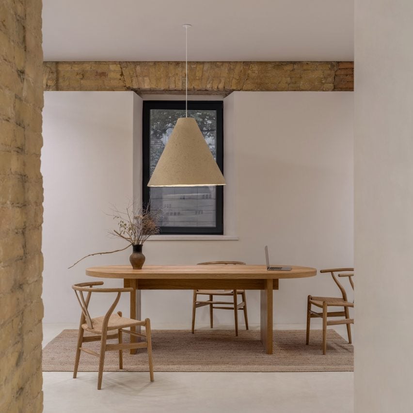 Photograph of a minimalist interior, showing a large wooden dining table with wishbone chairs and a large hanging pendant lamp.