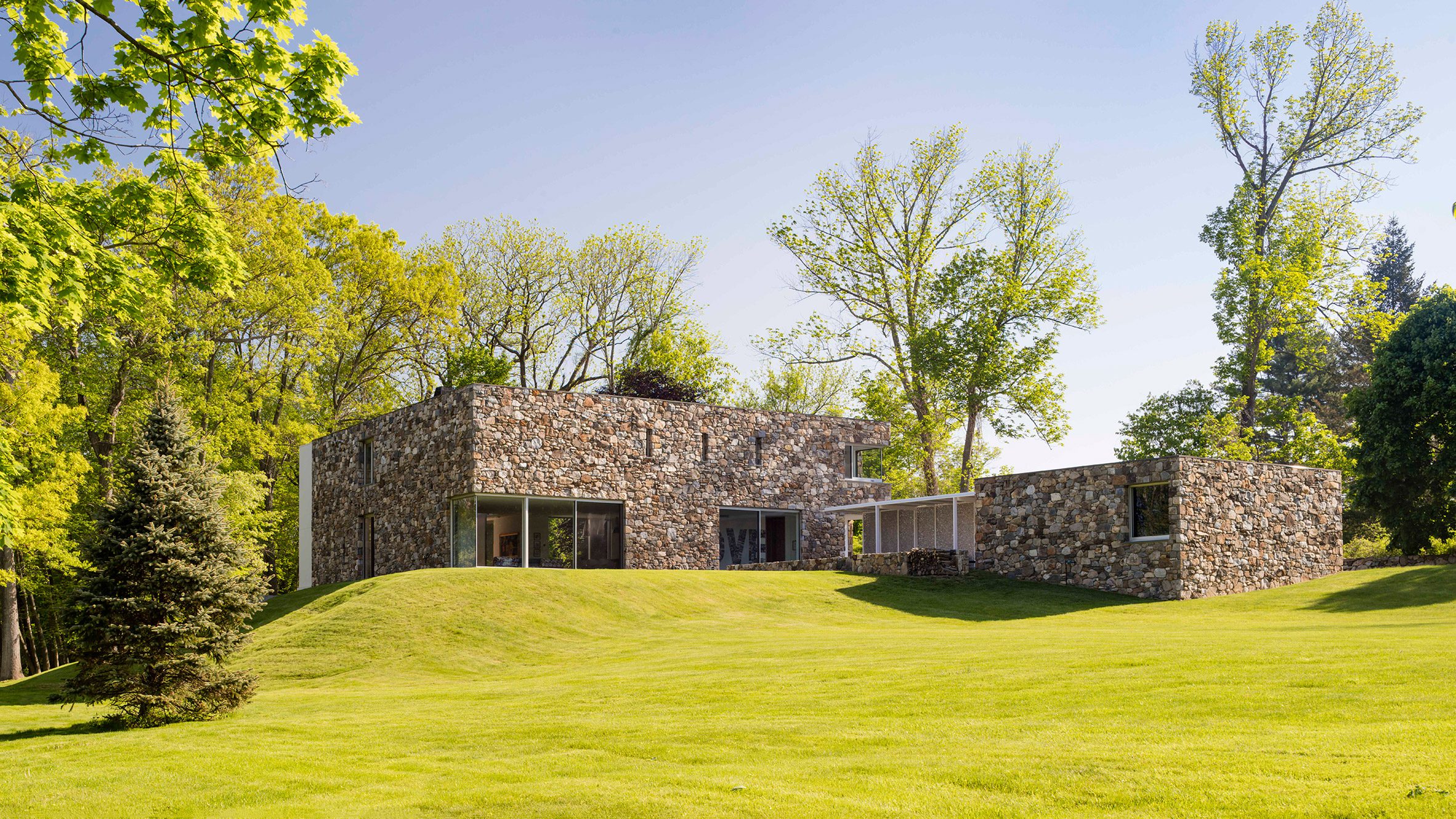 Photograph of a modern stone building situated on a hill, surrounded by trees.