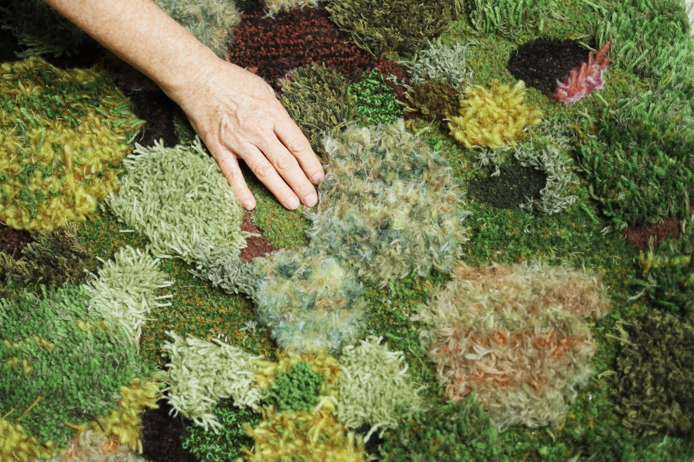 A photograph of a person's hand touching a soft, textured surface, in tones of green, brown and black.