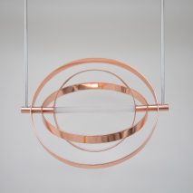 A photograph of a hanging circular metal installation in copper tones.