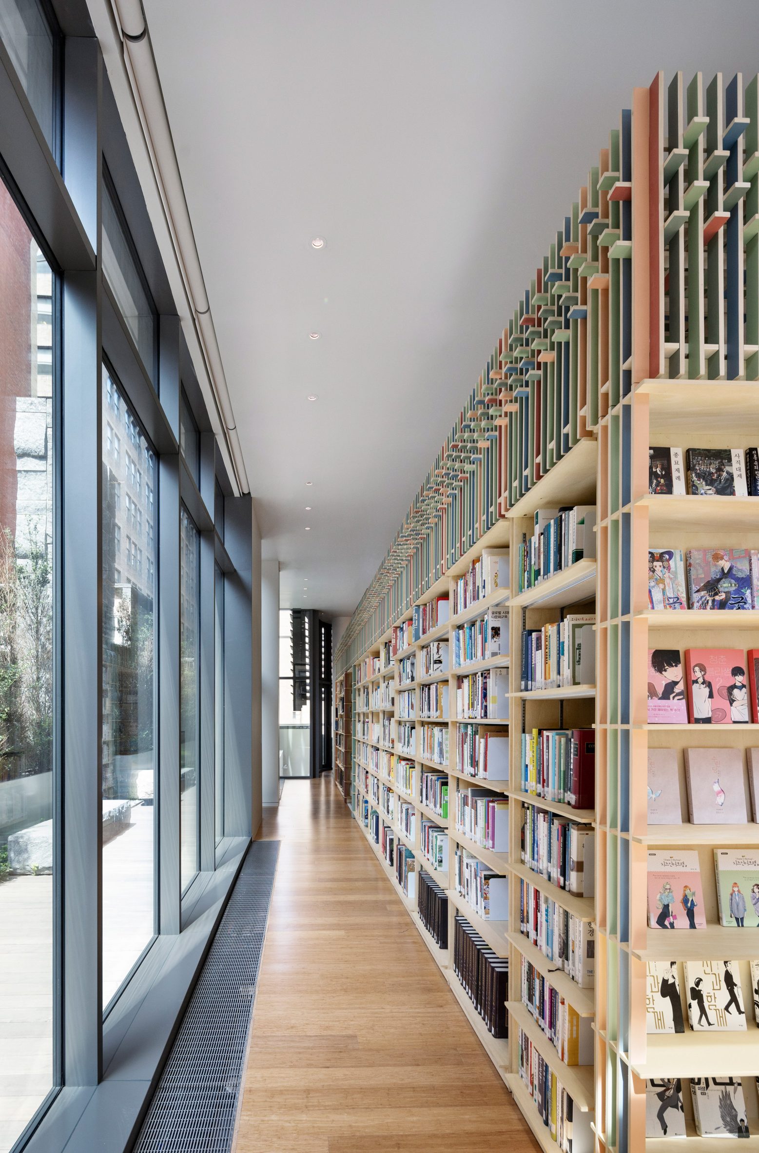 Corridor between a glass wall and a wooden bookshelf