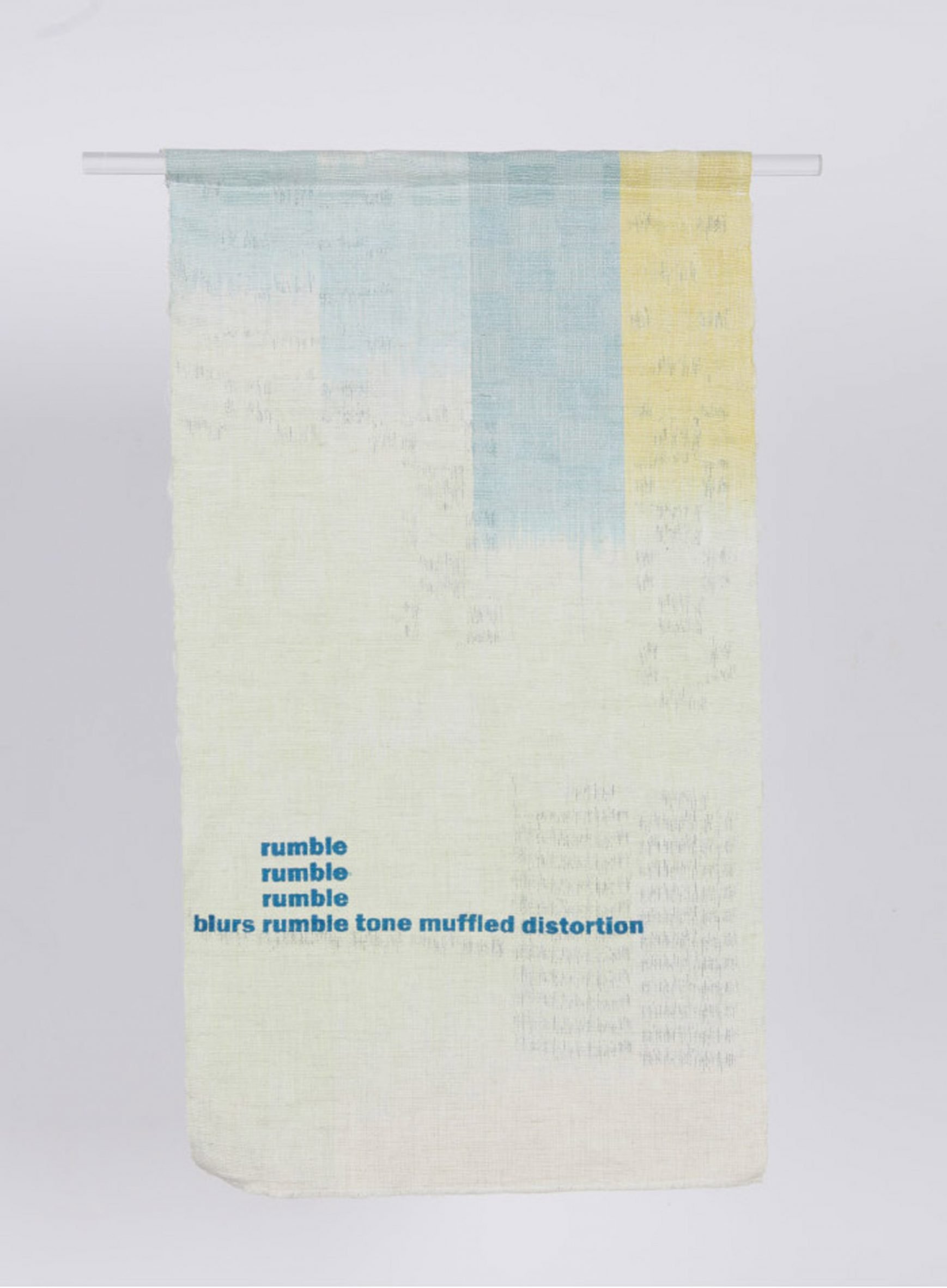 A photograph of a sheet of fabric hanging from a bar, in tones of blue and yellow. There is blue text printed onto the fabric that reads the text 'rumble', and 'blurs rumble tone muffled distortion'.