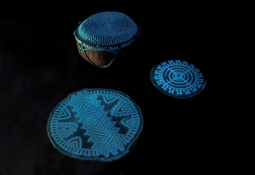 Photo of a traditional coconut-based drum covered in a patterned, glowing blue-green material on top, photographed in the dark