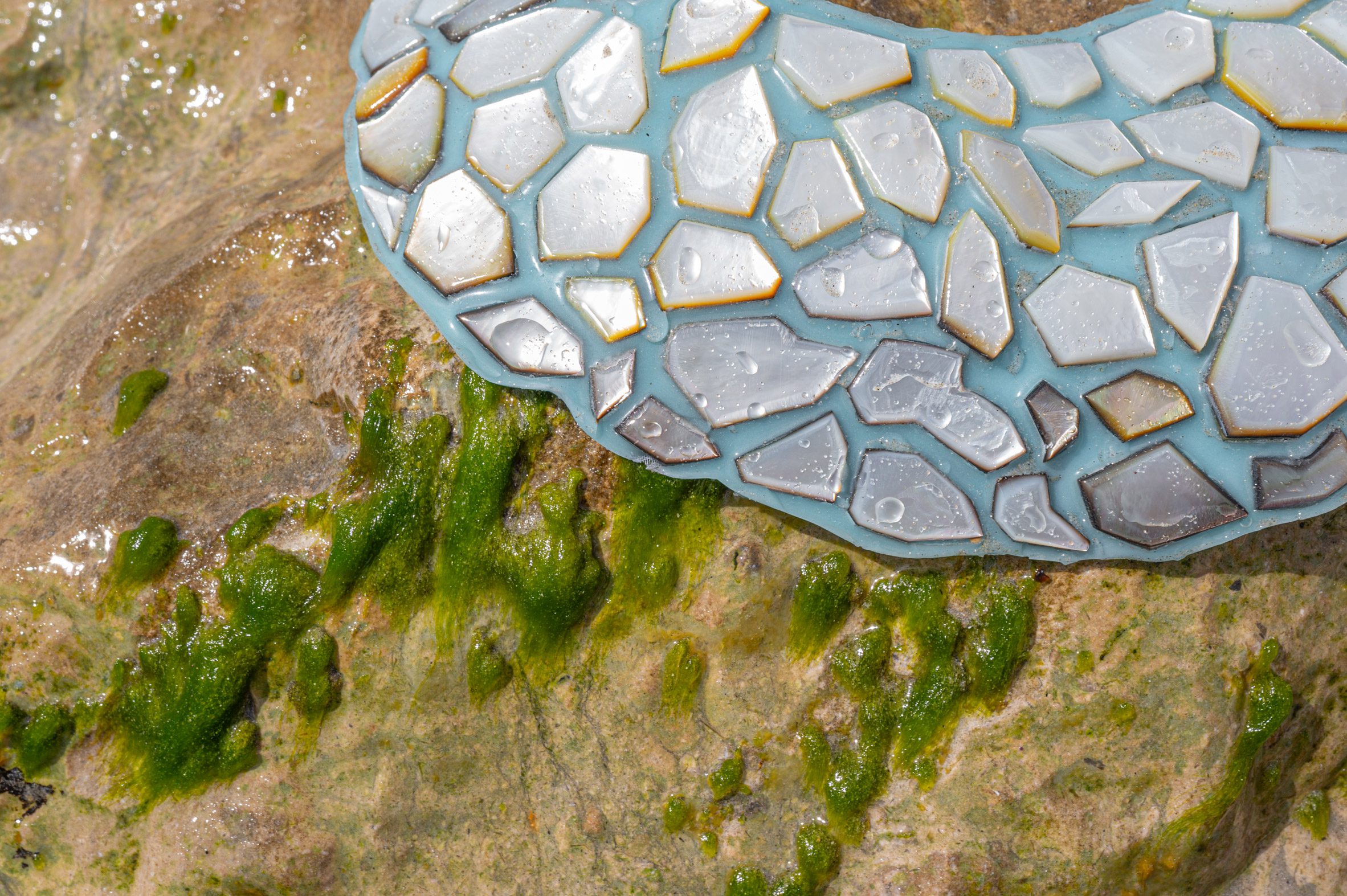 Close-up photo of a large piece of neck jewellery with mother of pearl fragments on a pale blue-green background