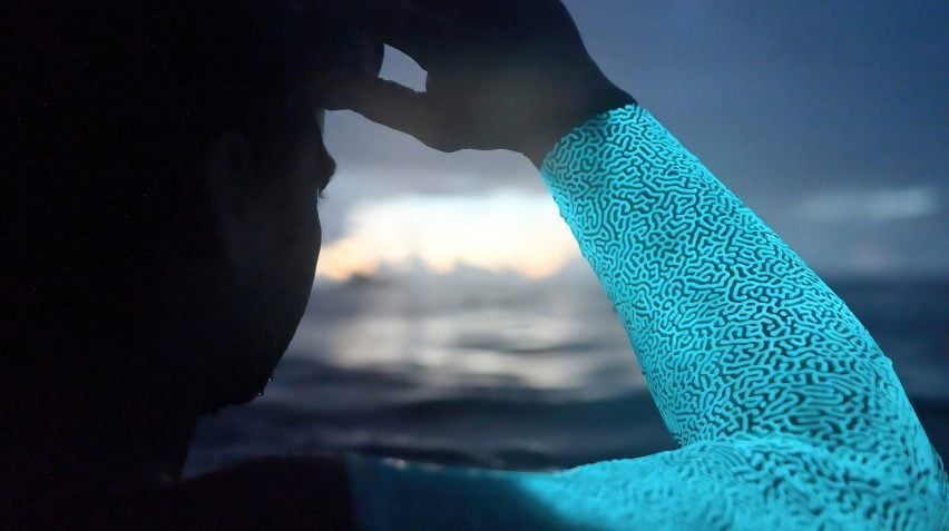 Close-up photo of a person's arm clothed in a skin-tight luminescent patterned swimsuit as they look out to sea