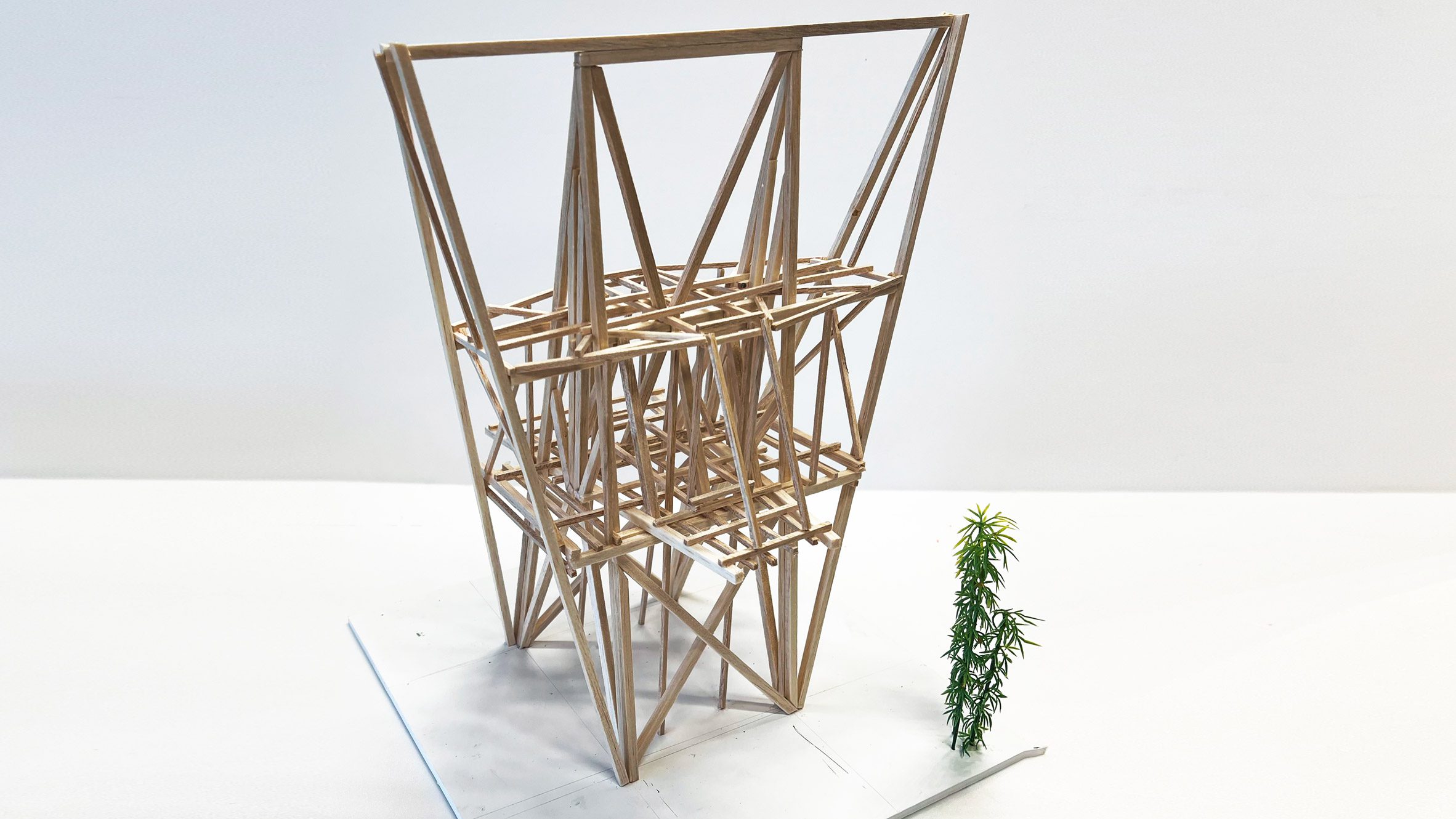 A photograph of an architectural model made from brown wooden sticks, in a geometric shape, against a white backdrop.