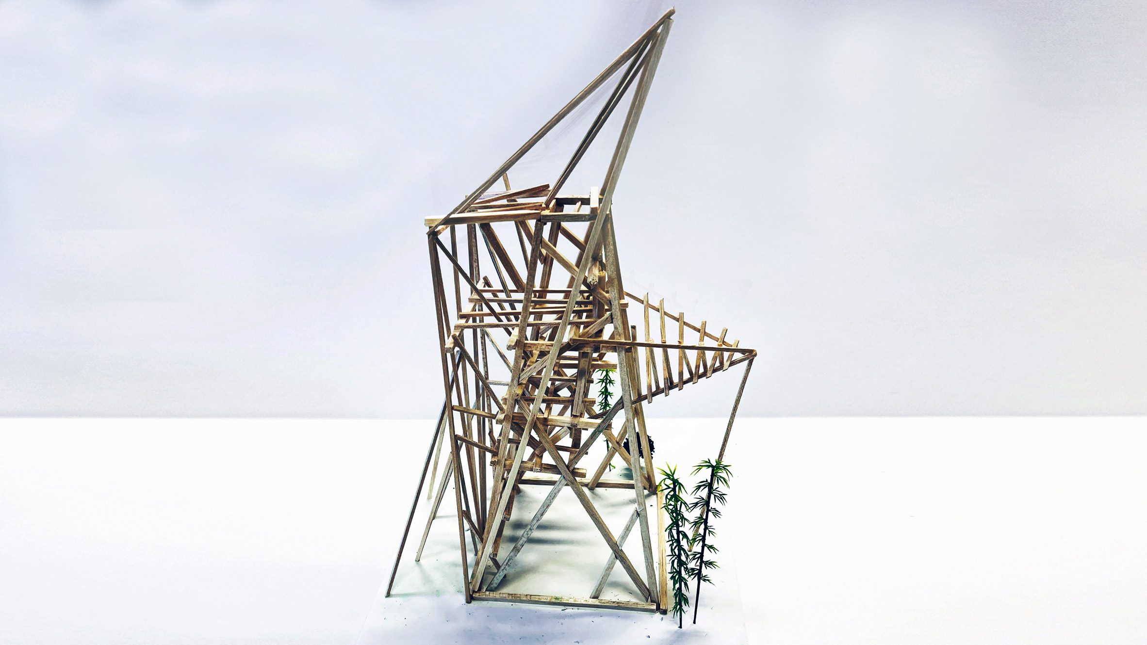 A photograph of an architectural model made from brown wooden sticks, in a geometric shape, against a white backdrop.