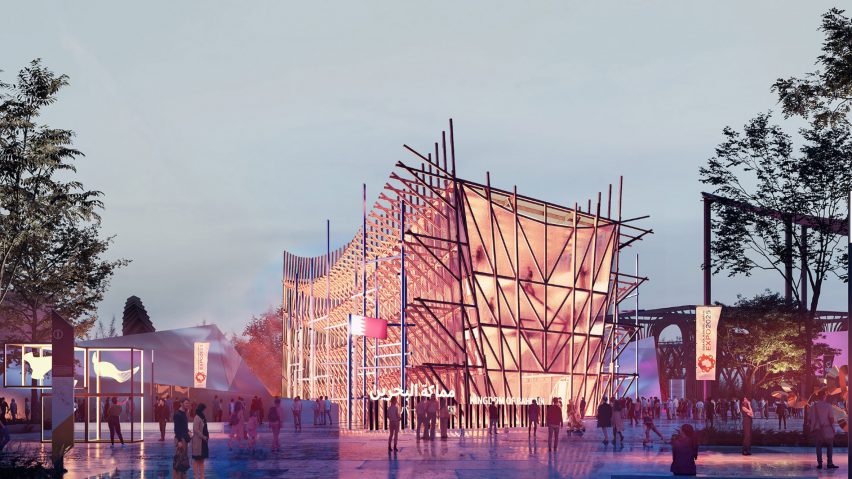 A photograph of an illuminated building in tones of pink, amongst a street with multiple people around it and a grey sky above.