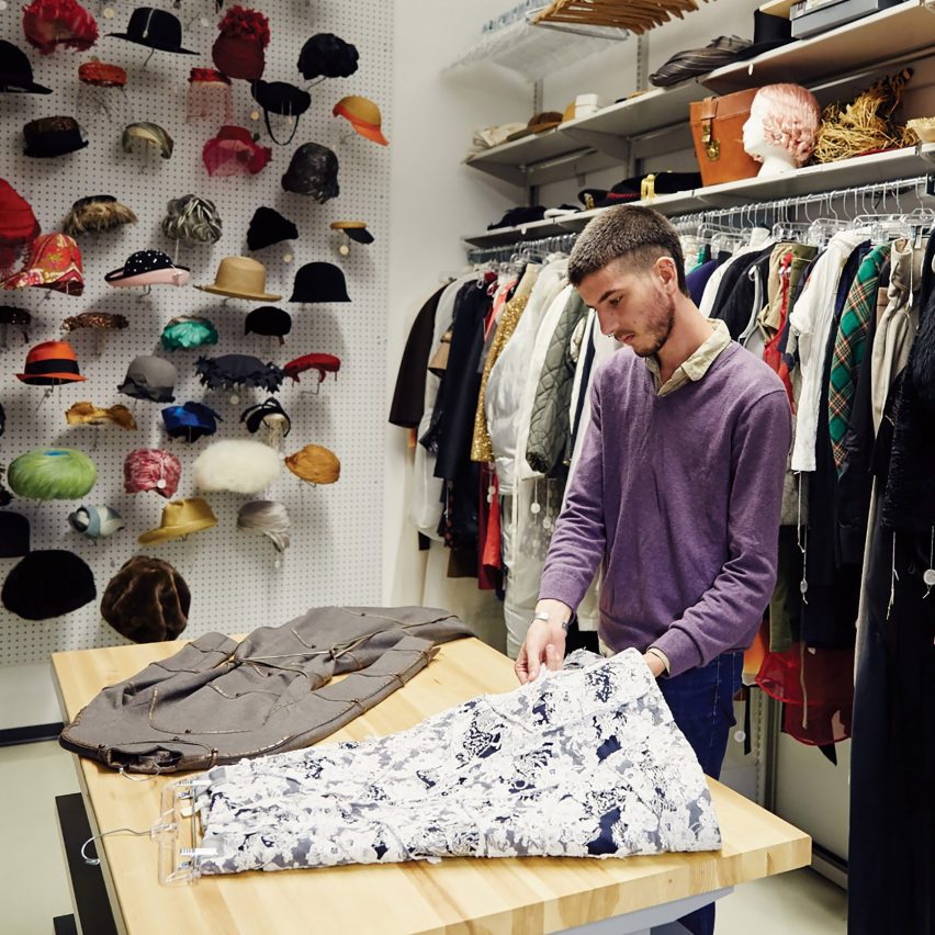 a photograph of a person holding garments, surrounded by clothes rails