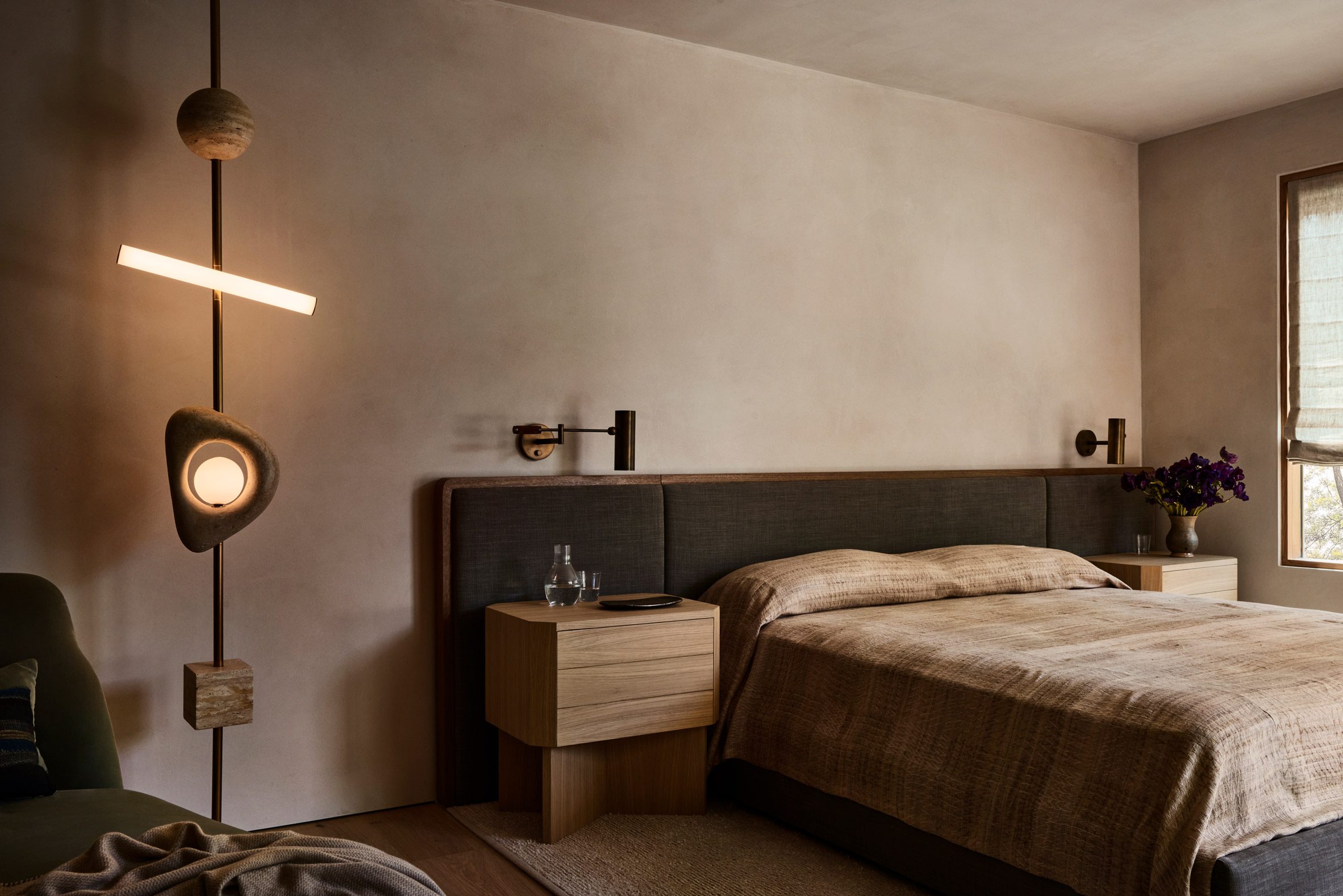 Sculptural light fixture running floor to ceiling in a neutrally decorated bedroom