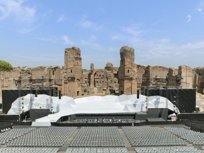 Photo of a stark, angular, large white stage in front of the ruins of the Baths of Caracalla in Rome