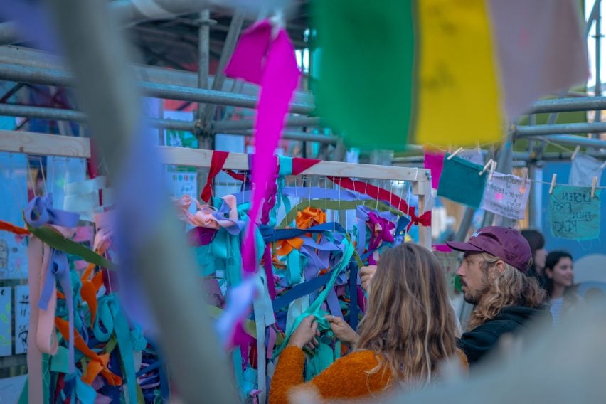 People tying lengths of fabric to strings on a frame