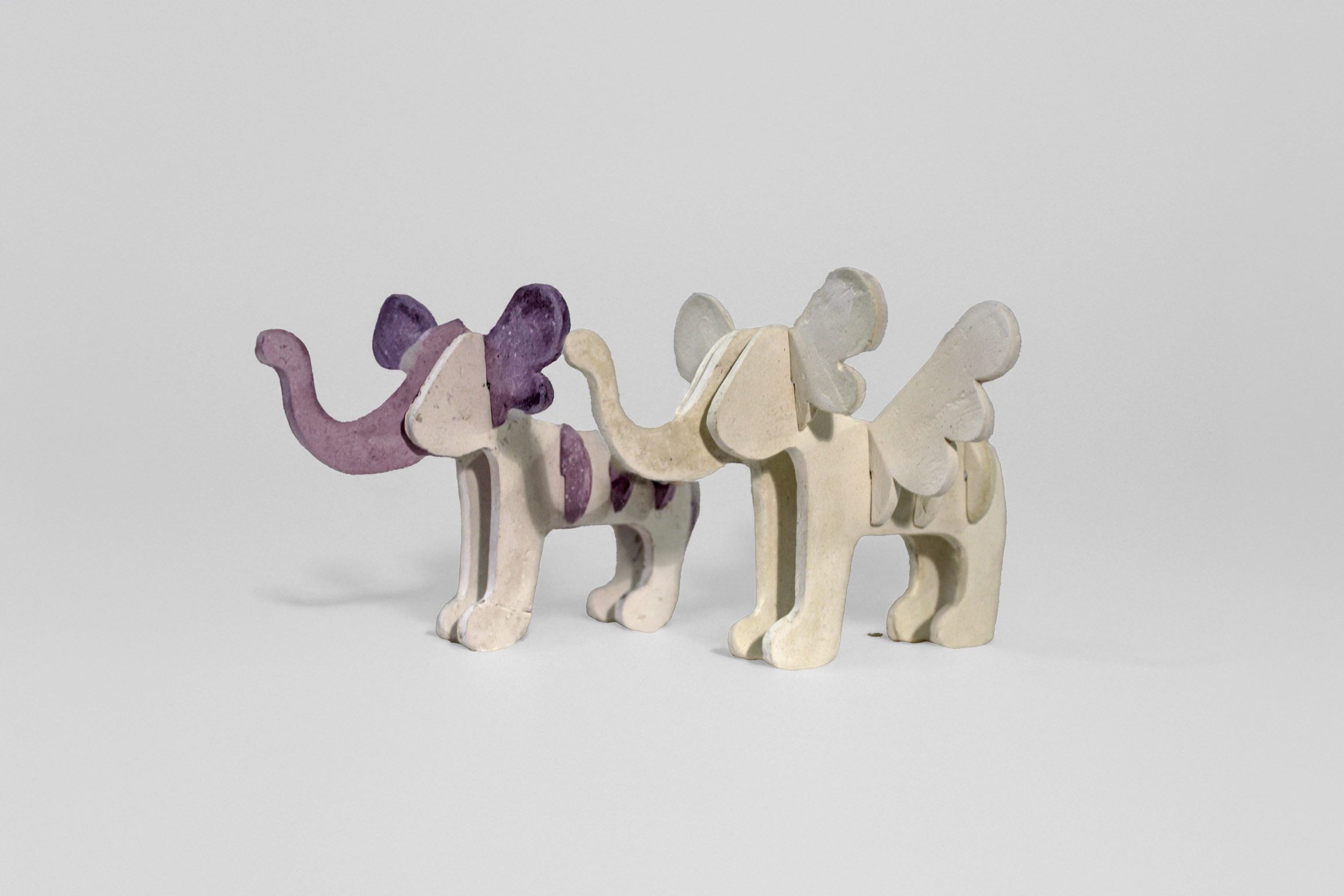 A photograph of two wooden toys shaped like elephants and in tones of purple and beige.