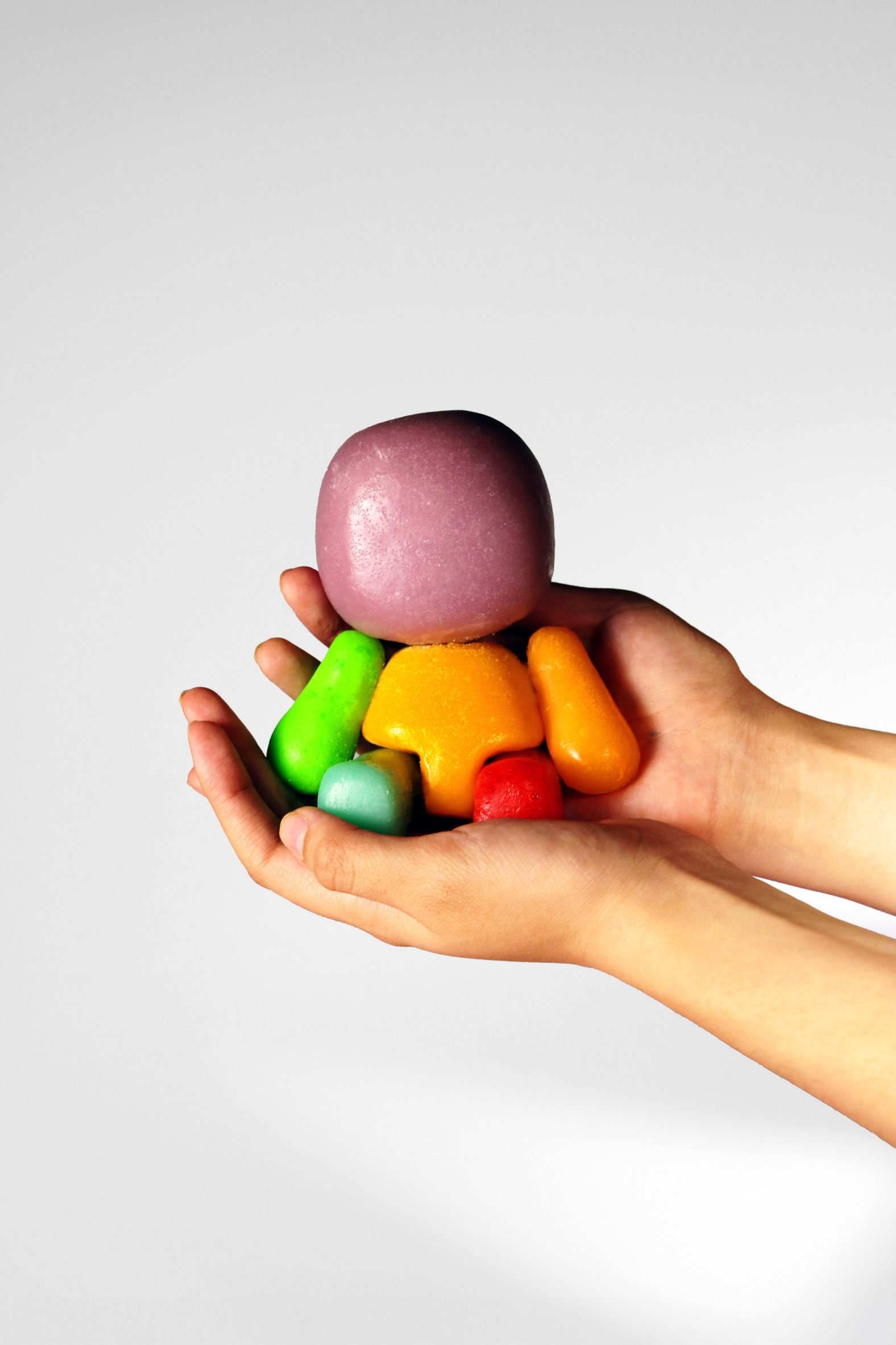 A photograph of a person's hands holding multicoloured circular toys in tones of green, orange, purple and red.