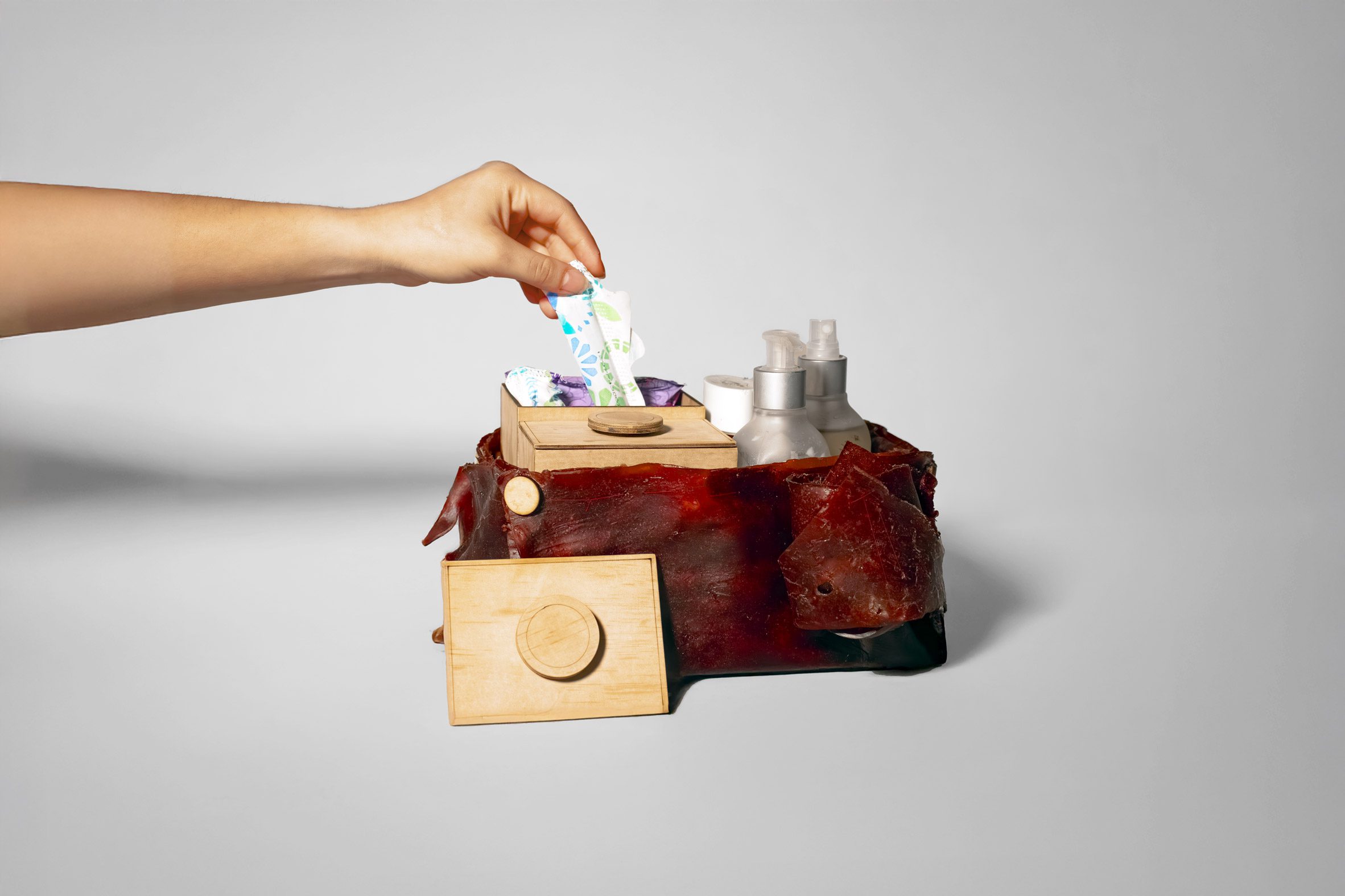 A photograph of a red box which holds menstrual products. There is a person's hand taking products out of the box.