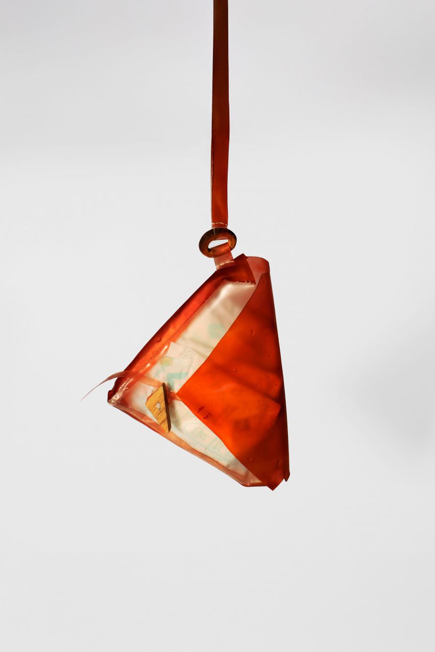 A photograph of a bag suspended in mid air, in tones of red and orange, against a grey backdrop.