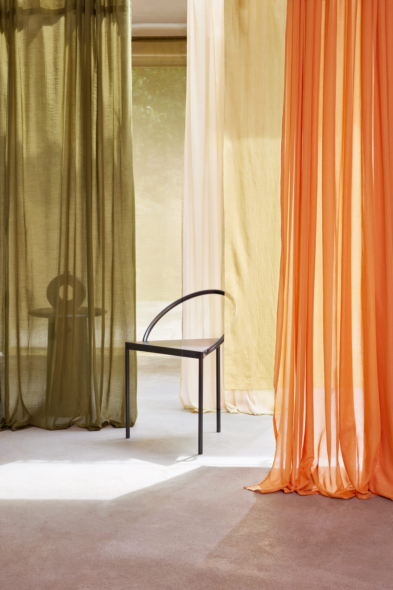 Photo of Kikrby Design's Aloe vera fabric hanging in long curtains in a room in an olive green, light cream and bright orange colour