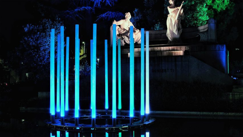 A photograph of a light installation in tones of blue, with white statues behind it in the distance.