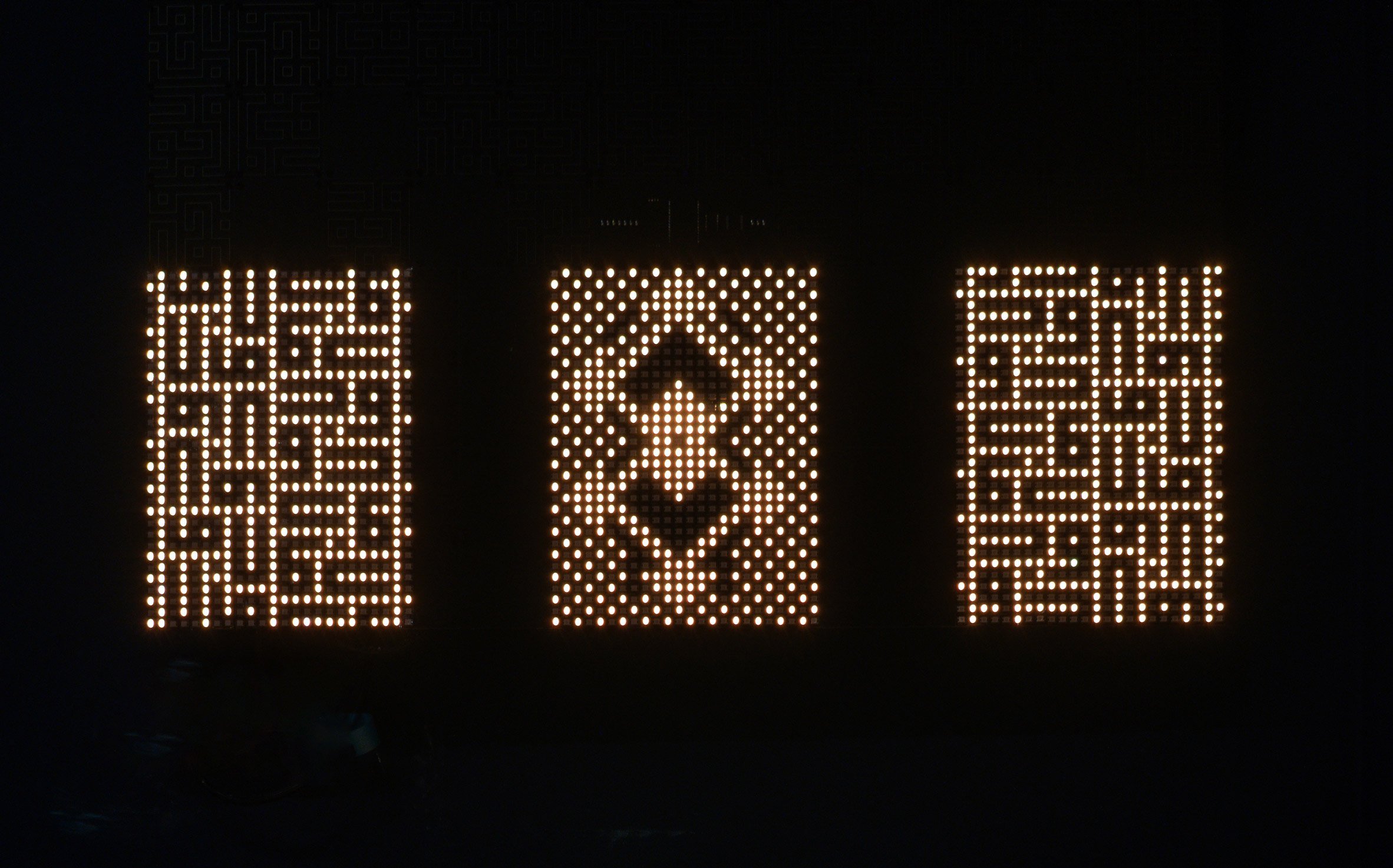 A photograph of a lighting installation, which consists of three rectangles with different illuminated patterns inside them, surrounded entirely by black.