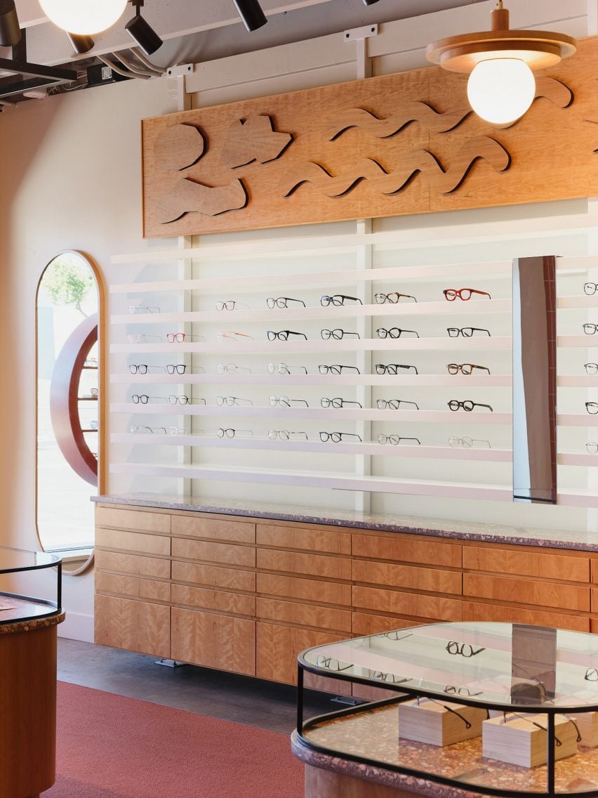 Eyewear displayed on minimalist white shelves below a cherry wood relief mural