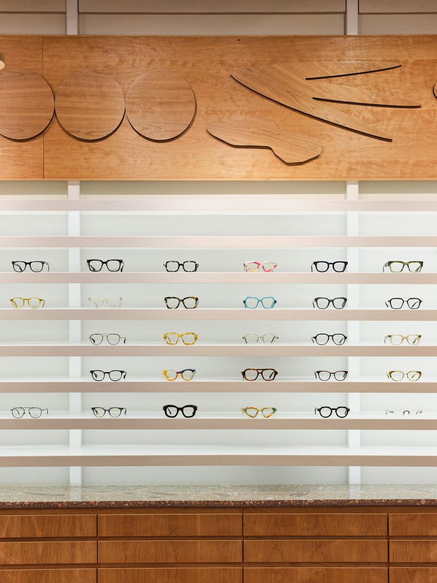 Eyewear displayed on minimalist white shelves below a cherry wood relief mural